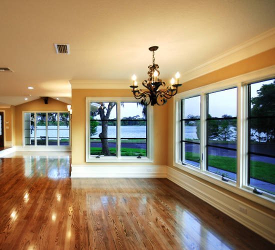 Sala luminosa con pisos de madera, candelabro y ventanas frente al lago